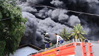 Petugas pemadam kebakaran berupaya memadamkan kobaran api yang membakar pabrik karet.